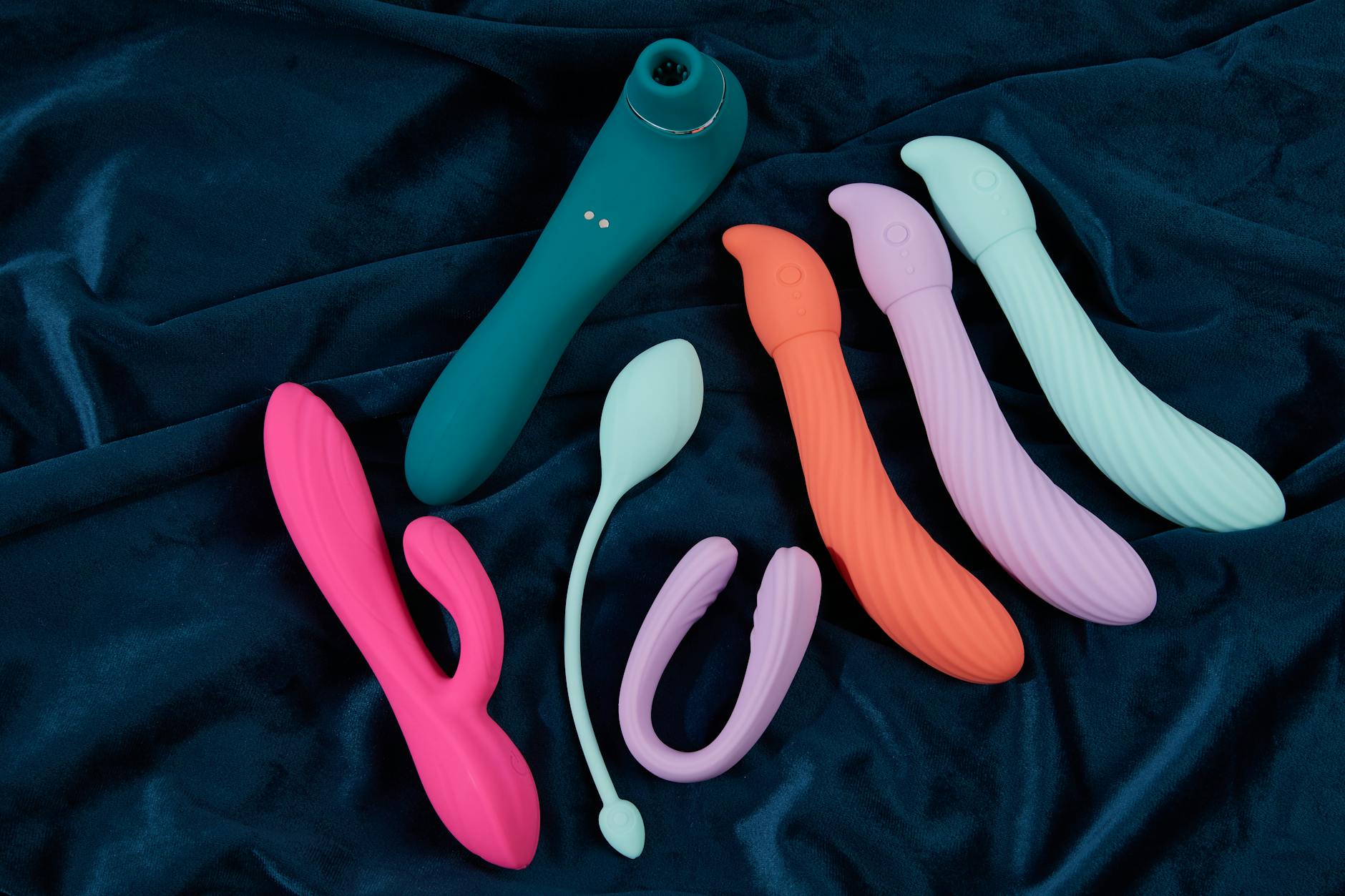 Silicone clitoral toys arranged on dark fabric, showing various textures and colors for different sensations