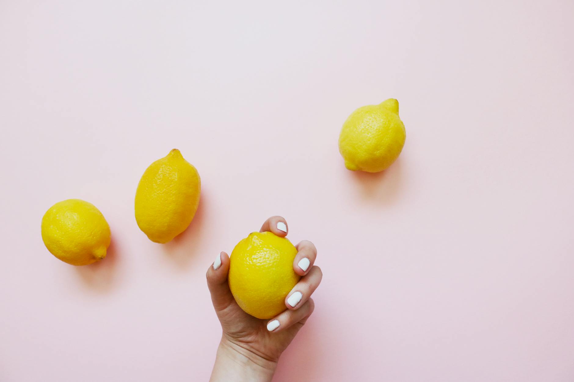 A hand holding a lemon against a soft pink background, symbolizing reconnection and freshness after time apart