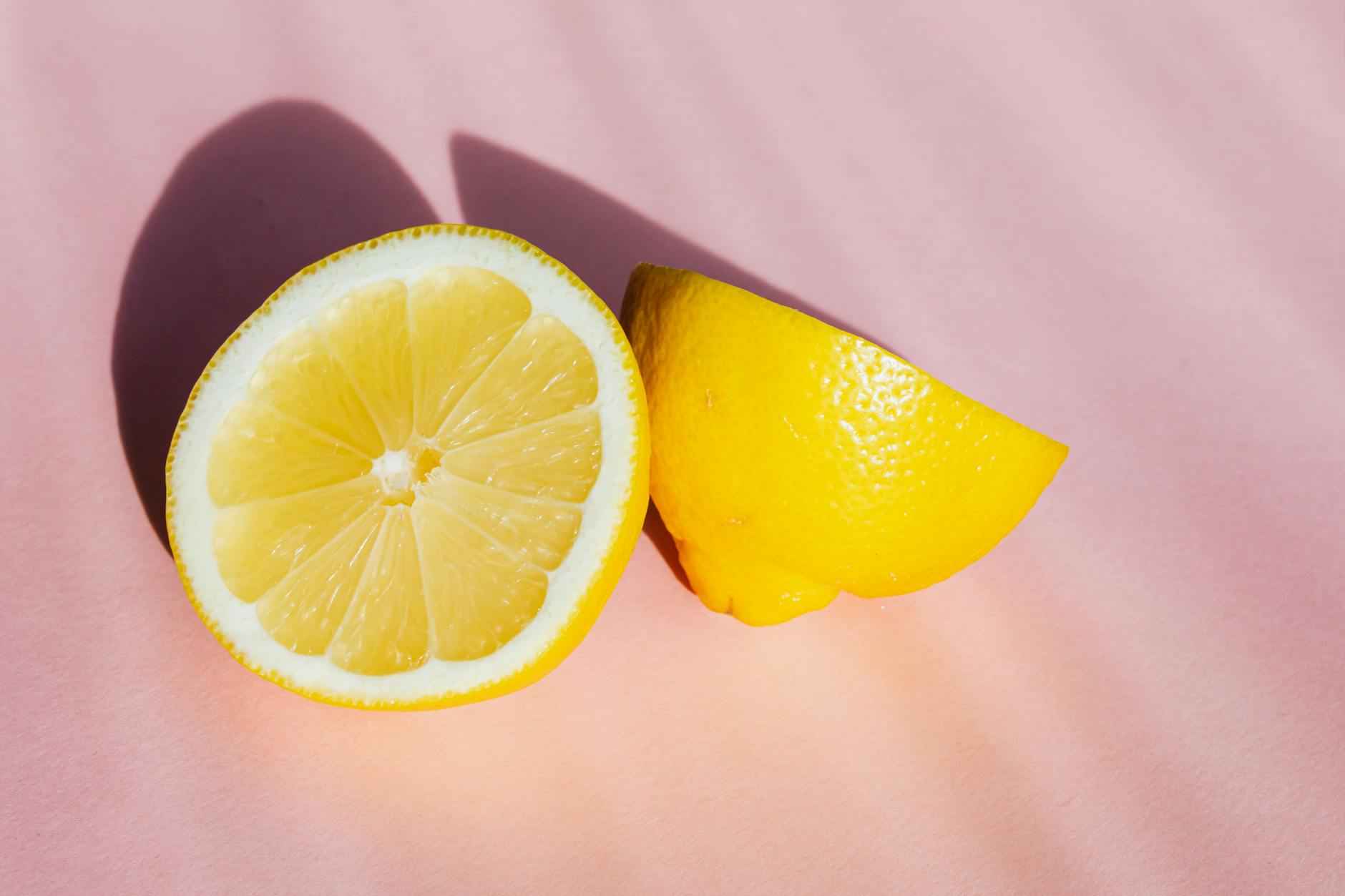 Fresh cut lemon halves on pink background in sunlight