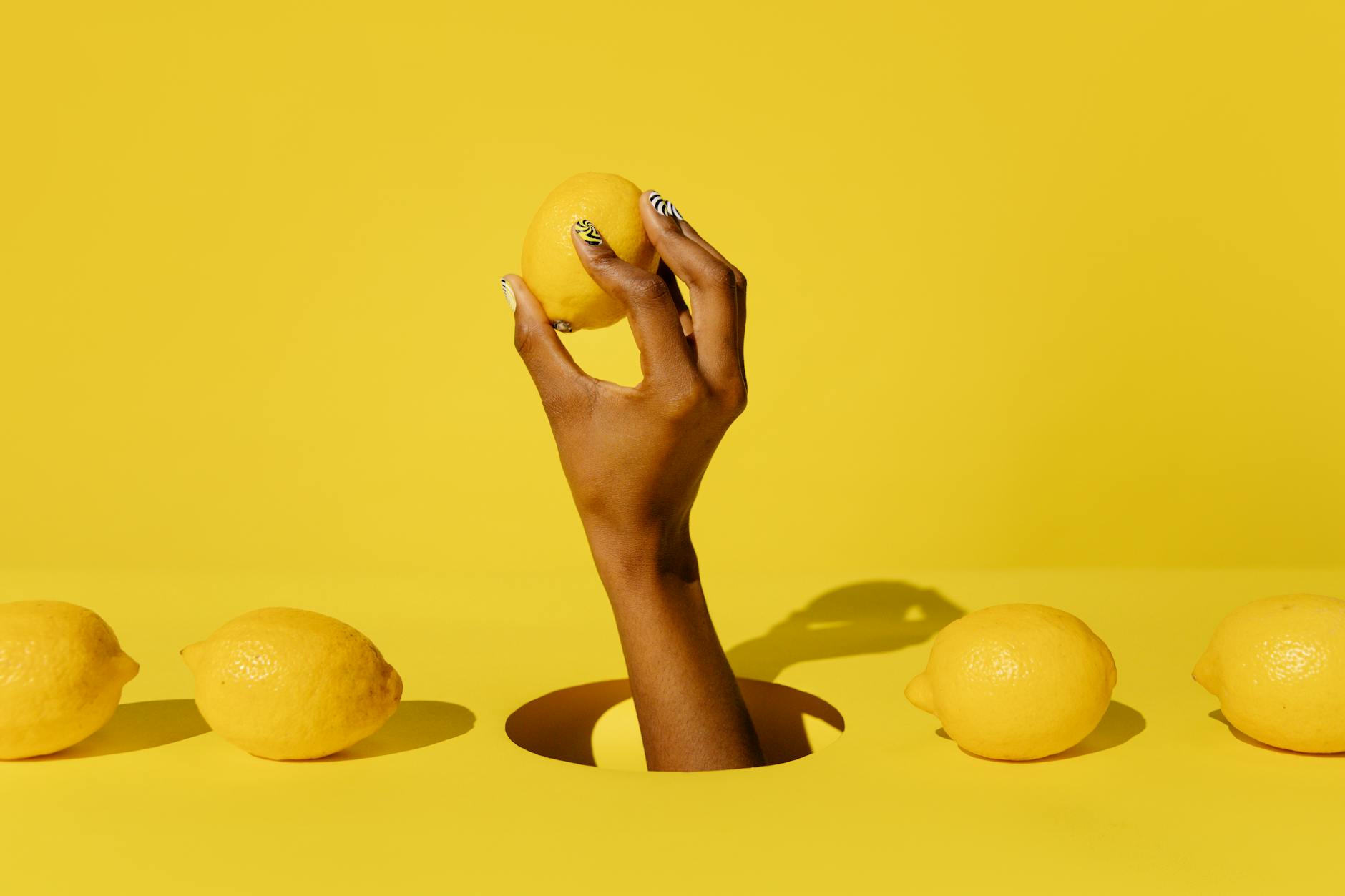 A hand holding a fresh lemon against a bright yellow background, symbolizing renewed energy and sensuality