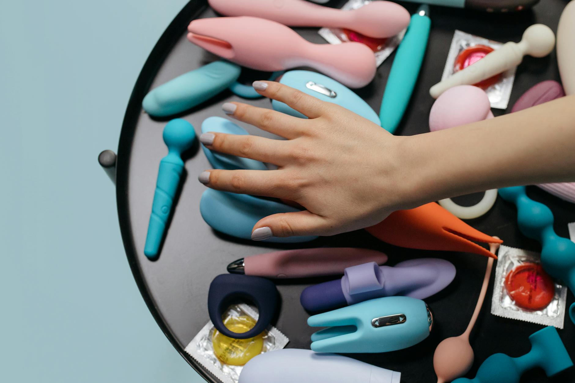 A hand reaching over a colorful arrangement of clitoral vibrators and toys on a table.