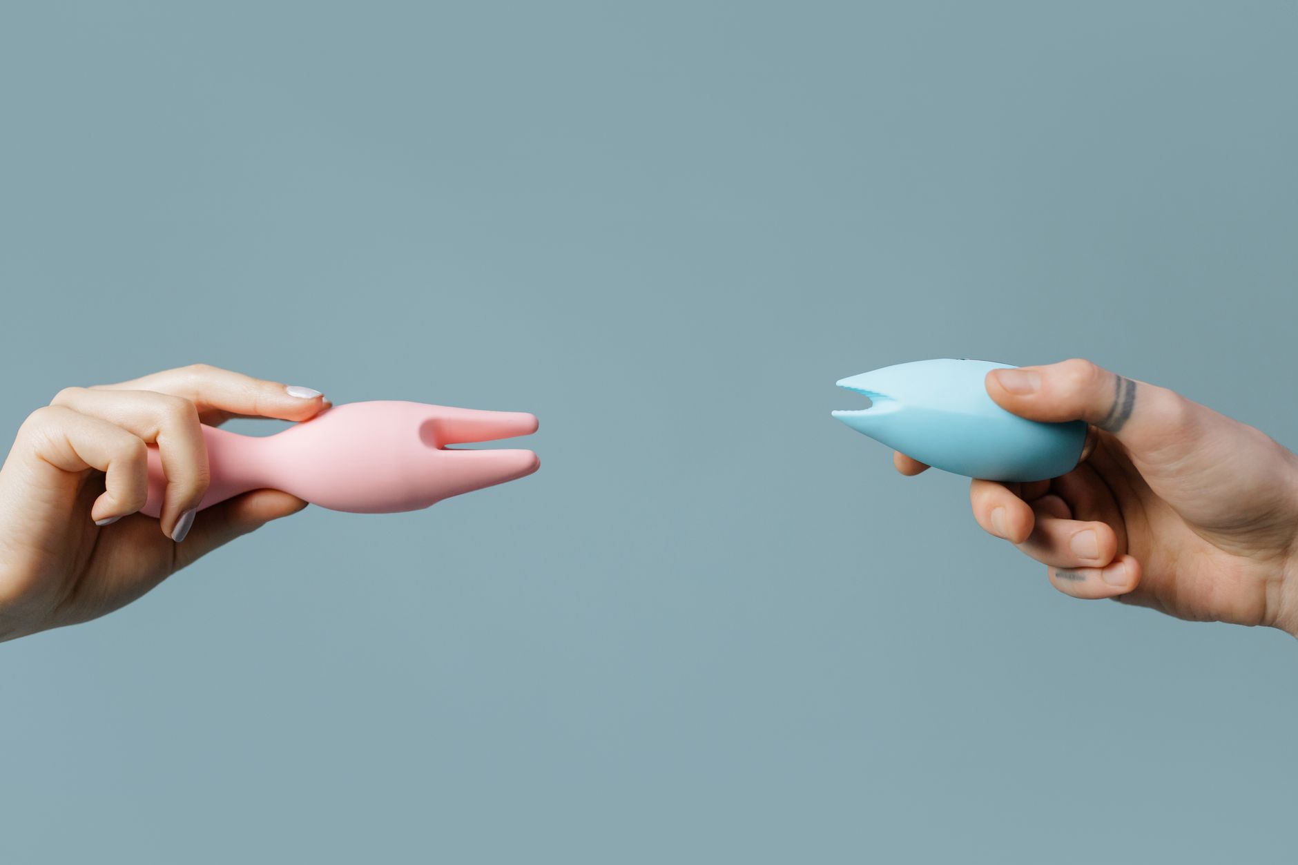 Two hands holding vibrators against a pastel background, symbolizing pleasure and self-exploration.