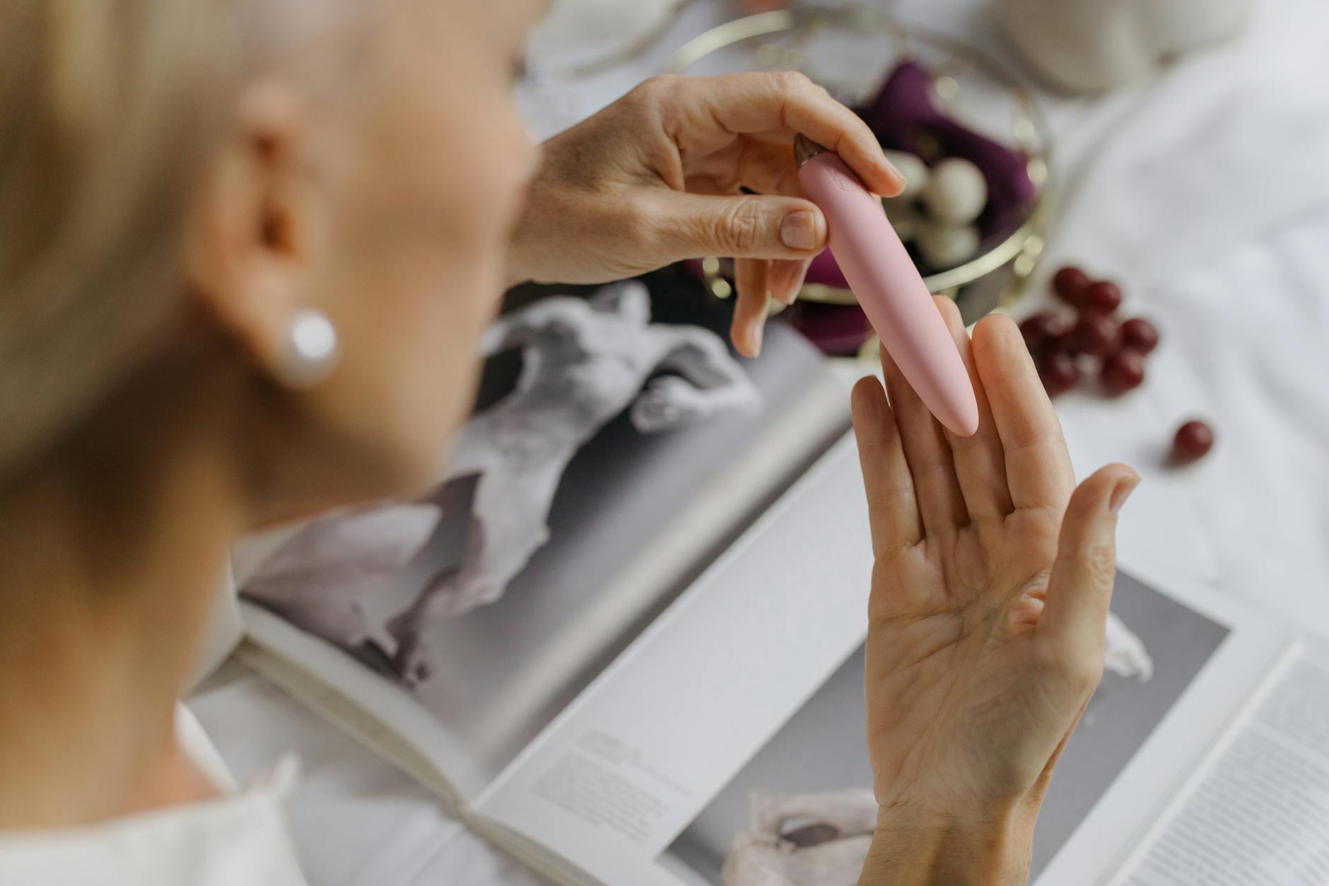 Mulher segurando vibrador rosa, com livros de arte ao fundo