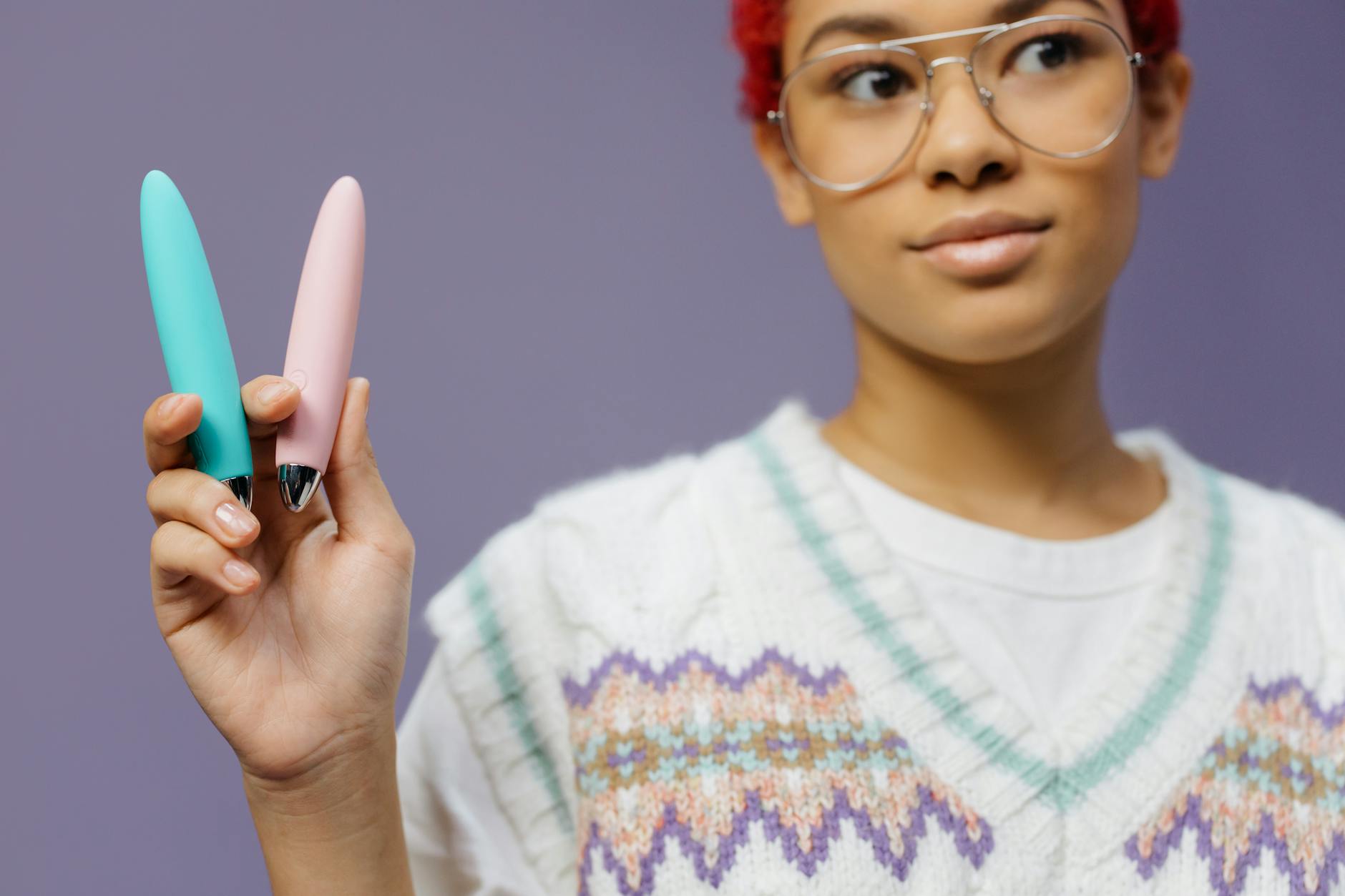 Mãos segurando um vibrador azul pessoal de massagem contra um suéter de tricô