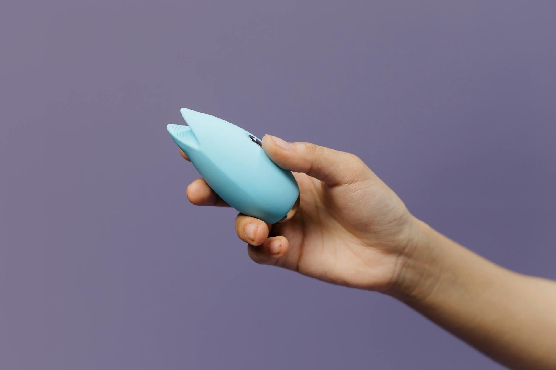 A silicone clitoral vibrator held in hand against a purple background, representing self-care during stressful periods
